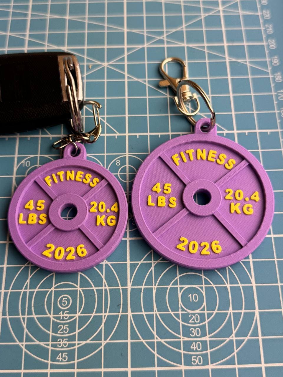 Purple and yellow Fitness Plate Keychain 3D prints on a cutting mat